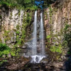 La plus belle cascade du Puy-de-Dôme, une chute d'eau double tombant sur des rochers escarpés, entourée de verdure luxuriante. Un arc-en-ciel apparaît dans la brume.