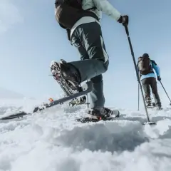 Deux personnes font une randonnée hivernale en raquettes sur un paysage enneigé sous un ciel bleu clair.