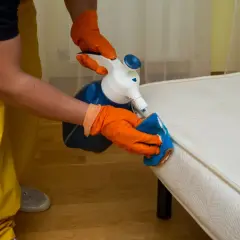 Personne en gants orange nettoie un matelas avec un spray et une éponge. Apprenez comment nettoyer un matelas gonflable efficacement.