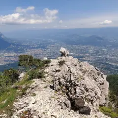 Vue panoramique depuis le sommet rocheux du Moucherotte, dominant une ville étendue sous un ciel bleu parsemé de nuages.