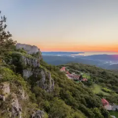 Vue panoramique d'un coucher de soleil sur la mer Adriatique, avec des ruines de château et des villages sur les pentes verdoyantes, sur le sentier Alpe Adria.