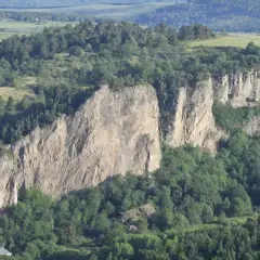 Falaises rocheuses spectaculaires, idéales pour une randonnée à Murol. Végétation luxuriante et paysage vallonné en arrière-plan.