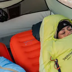 Une personne dort dans une tente sur deux matelas superposés. Le matelas du bas est orange, celui du dessus est bleu.