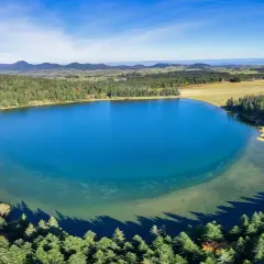 Vue aérienne du lac de Servièressurrounded par une forêt de pins. Le ciel est bleu clair avec quelques nuages.