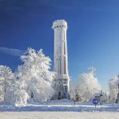 Tour de guet enneigée, tel un champ du feu blanc sous un ciel bleu intense. Arbres givrés et paysage hivernal.