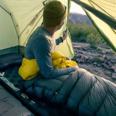Un campeur, dans sa tente, tient un sac de couchage jaune. Il est temps de savoir comment ranger un sac de couchage pour le prochain voyage.