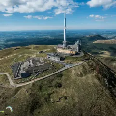 Vue aérienne du Puy de Dôme dans le Massif Central, avec sa tour de télécommunication et des parapentistes profitant du paysage.