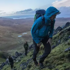 Randonneurs sur un sentier escarpé du Skye Trail, profitant d'un paysage spectaculaire avec des lacs et la mer en arrière-plan.
