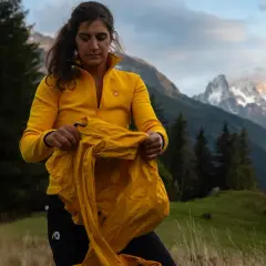 Une randonneuse en jaune prépare ses affaires, prête pour une aventure en montagne. Ses 3 couches randonnée sont essentielles pour affronter le climat changeant.