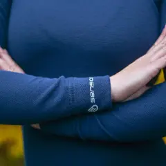 Une personne porte un pull bleu marine en laine mérinos, doux et chaud. Le logo "Sensor" est visible sur le poignet.