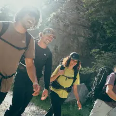 Quatre randonneurs souriants avancent sur un sentier. Le poids du sac à dos en randonnée semble léger pour ce groupe joyeux.