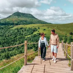 Couple se promenant sur un sentier en bois, admirant les plus beaux endroits d'Auvergne, avec le Puy de Dôme en arrière-plan.