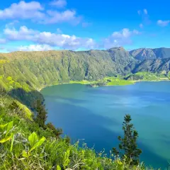 Vue panoramique sur le lac d'une beauté saisissante à São Miguel, entouré de montagnes verdoyantes sous un ciel bleu éclatant.