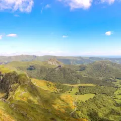 Magnifique panorama du Puy Mary, avec ses crêtes verdoyantes et ses vallées boisées sous un ciel bleu éclatant.