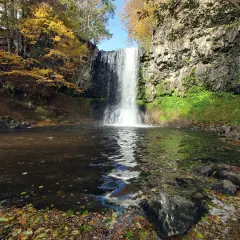 La cascade d'Entraigues, un rideau d'eau tombant dans un bassin entouré de roches et de feuillages d'automne aux couleurs vives.