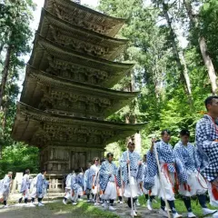 Marche d'hommes en tenue traditionnelle, portant des bâtons, devant une pagode à cinq étages, dans le cadre d'une cérémonie Dewa Sanzan.