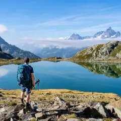 Randonneur contemplant un lac d'altitude aux reflets parfaits, paysage du tour des lacs des 7 Laux.