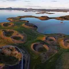 Paysage spectaculaire du lac Myvatn en Islande, avec ses cratères volcaniques verdoyants et ses eaux calmes reflétant le ciel.