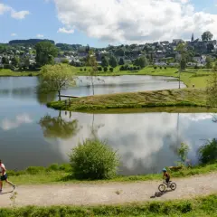 Un homme court sur le sentier, un enfant fait du vélo près du lac tour d'auvergne. Village en arrière-plan.