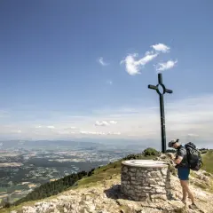Fin d'une randonnée boucle 5 jours Jura. Un randonneur admire le panorama depuis un sommet, près d'une croix et d'un repère.