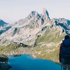 Randonneuse admirant un lac bleu et des montagnes majestueuses, un refuge en vue. Une belle étape du tour du Beaufortain 3 jours.