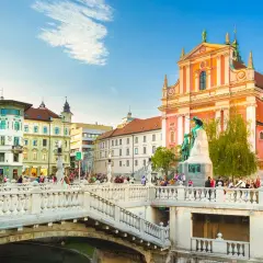 Pont triple de Ljubljana, un incontournable Slovénie, avec l'église franciscaine rose et des passants profitant du soleil.