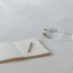 Un carnet ouvert avec un stylo doré et une gourde en verre. Idéal pour noter ses pensées et s'hydrater, sans enlever le goût plastique de la gourde.