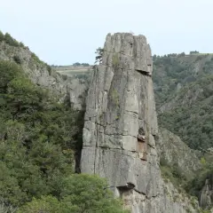 Un piton rocheux domine les gorges du Bes, entouré de végétation luxuriante et de falaises escarpées.