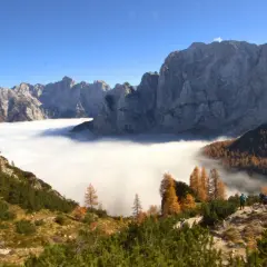 Vue spectaculaire des Alpes Juliennes, avec une mer de nuages enveloppant les vallées et des montagnes majestueuses sous un ciel bleu.
