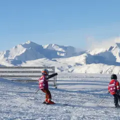 Enfants en plein cours de ski, profitant d'une journée ensoleillée avec des montagnes enneigées en arrière-plan.