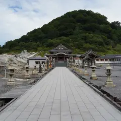 Allée de lanternes menant à un temple au pied du mont Osore, paysage volcanique et verdoyant.