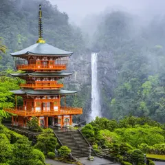 Pagode à trois étages de couleur orange vif, niché dans une végétation luxuriante sur la péninsule de Kii, avec une cascade majestueuse en arrière-plan.