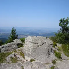Vue panoramique depuis le sommet rocheux, un sentier serpente à travers la végétation. Le testavoyre offre un paysage de montagnes et de vallées sous un ciel bleu.