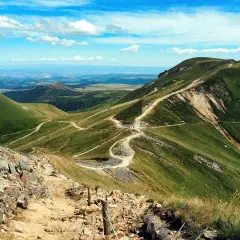 Sentier sinueux sur les pentes verdoyantes du Puy de Dôme, offrant une vue panoramique sur le village autour du Mont-Dore.