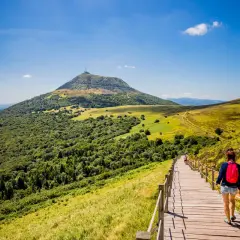 Une randonneuse sur un sentier en bois, profitant du paysage verdoyant du Massif Central. Le tourisme y est magnifique.