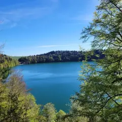 Vue magnifique d'une randonnée au lac Pavin, avec ses eaux bleues profondes entourées de forêts verdoyantes sous un ciel clair.