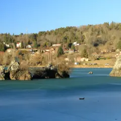 Le lac de Cassière gelé, avec ses îlots rocheux et ses maisons sur la colline boisée, sous un ciel bleu clair.