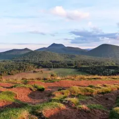 Vue panoramique sur les volcans d'Auvergne, avec le Puy Chopine dominant la forêt verdoyante sous un ciel nuageux.