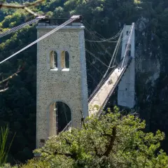 Le viaduc des Rochers Noirs, un pont suspendu impressionnant, traverse une vallée verdoyante. Deux personnes à vélo profitent de la vue.