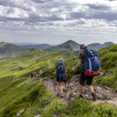 Randonneurs sur un sentier escarpé, dominant des paysages verdoyants et des volcans du puy May.