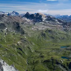 Vue panoramique des Alpes, avec le Mont Thabor en arrière-plan. Des lacs bleus scintillent dans la vallée verdoyante.