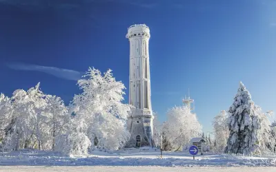 Tour de guet enneigée, tel un champ du feu blanc sous un ciel bleu intense. Arbres givrés et paysage hivernal.