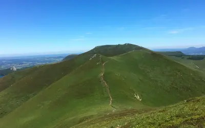 Sentier sinueux menant à la croix Morand, dominant un paysage verdoyant sous un ciel bleu.