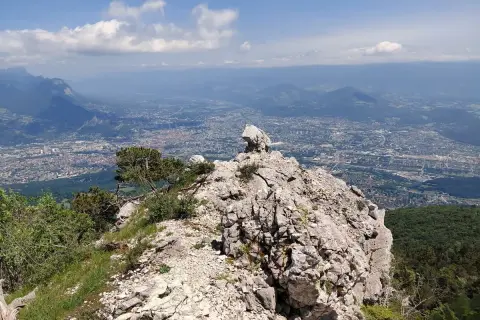 Vue panoramique depuis le sommet rocheux du Moucherotte, dominant une ville étendue sous un ciel bleu parsemé de nuages.
