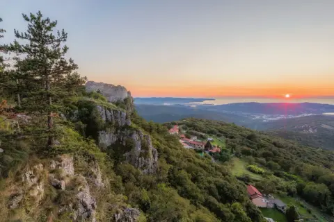 Vue panoramique d'un coucher de soleil sur la mer Adriatique, avec des ruines de château et des villages sur les pentes verdoyantes, sur le sentier Alpe Adria.