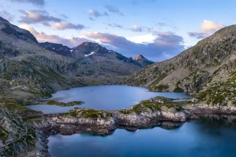 Vue aérienne du lac des 7 Laux, entouré de montagnes rocheuses et verdoyantes, sous un ciel aux teintes rosées.