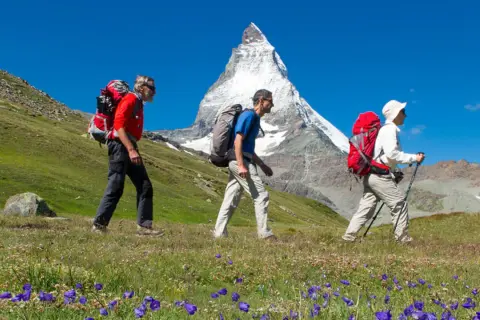 Randonneurs en marche avec le **Tour du Cervin** en toile de fond, sous un ciel bleu éclatant.