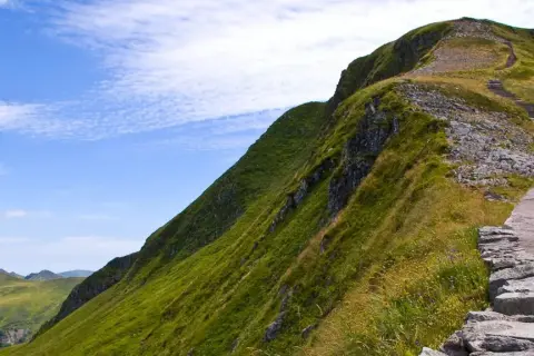Sentier de montagne verdoyant avec escaliers, idéal pour une randonnée gr pour débutant. Paysage spectaculaire sous un ciel bleu.