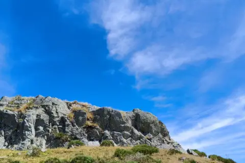 Rochers escarpés du Puy de Niermont sous un ciel bleu éclatant, parsemé de nuages légers.