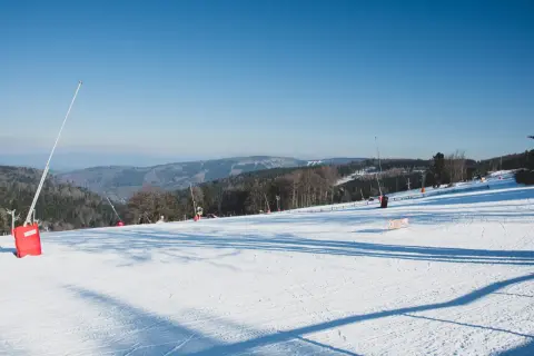 Piste de ski de fond au Champ du Feu, sous un ciel bleu. Des canons à neige sont visibles sur le flanc de la montagne enneigée.